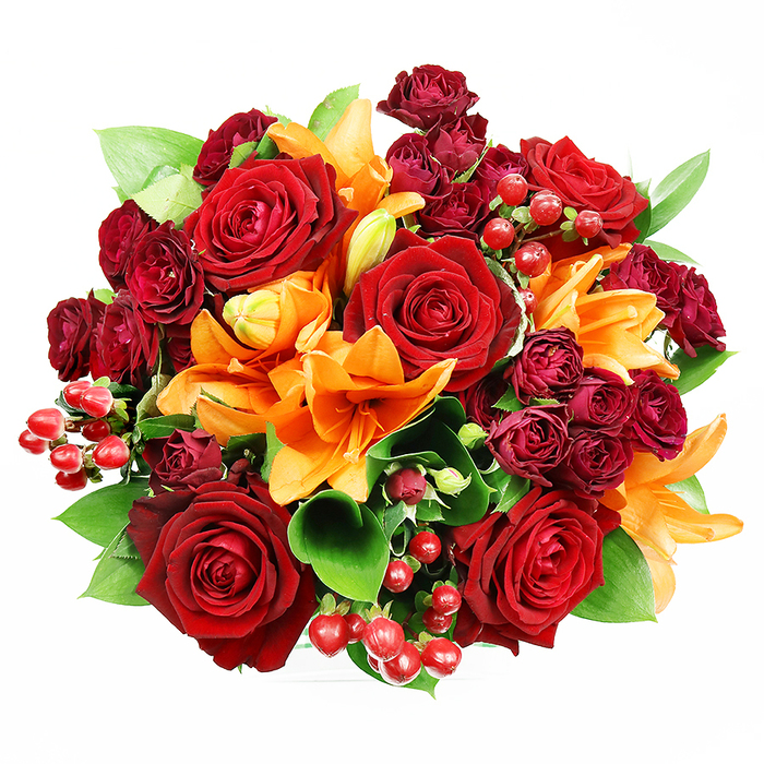 Captured from directly overhead on a crisp white backdrop, this densely composed, circular bouquet presents a refined interplay of colour and texture that reads like a small, wearable garden. Dominating the design are several large, deep-red roses with velvety, fully unfurled petals whose layered centers create a classic focal point. Interspersed are bright orange Asiatic lilies: some trumpet-shaped blooms lie open with their stamens and subtle spotting exposed, while others remain in elegant bud form, contributing rhythmic variation across the composition. Tucked in between these larger elements are tight clusters of dark burgundy spray roses, their miniature, clustered heads adding concentrated, velvety depth and a rich tonal undercurrent. Glossy hypericum berries in a true ruby red offer small, luminous points that catch the even studio light and introduce a pleasingly different surface to the soft blooms. The bouquet's greenery - smooth, broad leaves such as ruscus or salal - peeks out and frames the flowers, its fresh greens providing a crisp contrast that enhances each warm hue. The lighting is soft and flattering, revealing petal textures and the gentle sheen on the berries while keeping shadows minimal; the imagined scent is a layered combination of rose's warm sweetness and a faint spice from the lilies. This arrangement feels both luxurious and approachable: fitting for an anniversary, a romantic gesture, or as a striking centrepiece for a gathering after an afternoon stroll near Boxmoor or a market visit along The Marlowes in Hemel Hempstead.